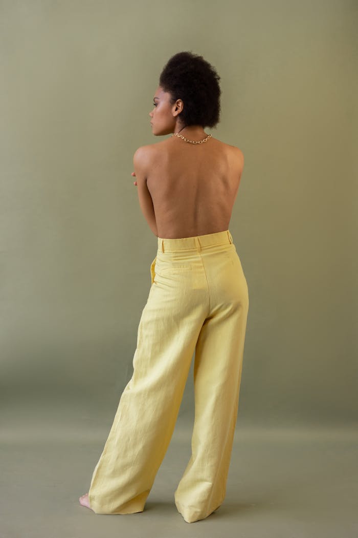 Studio portrait of a woman with an exposed back in stylish yellow pants.